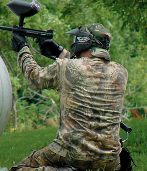 Joe Bechler squatting behind a propane tank aiming left